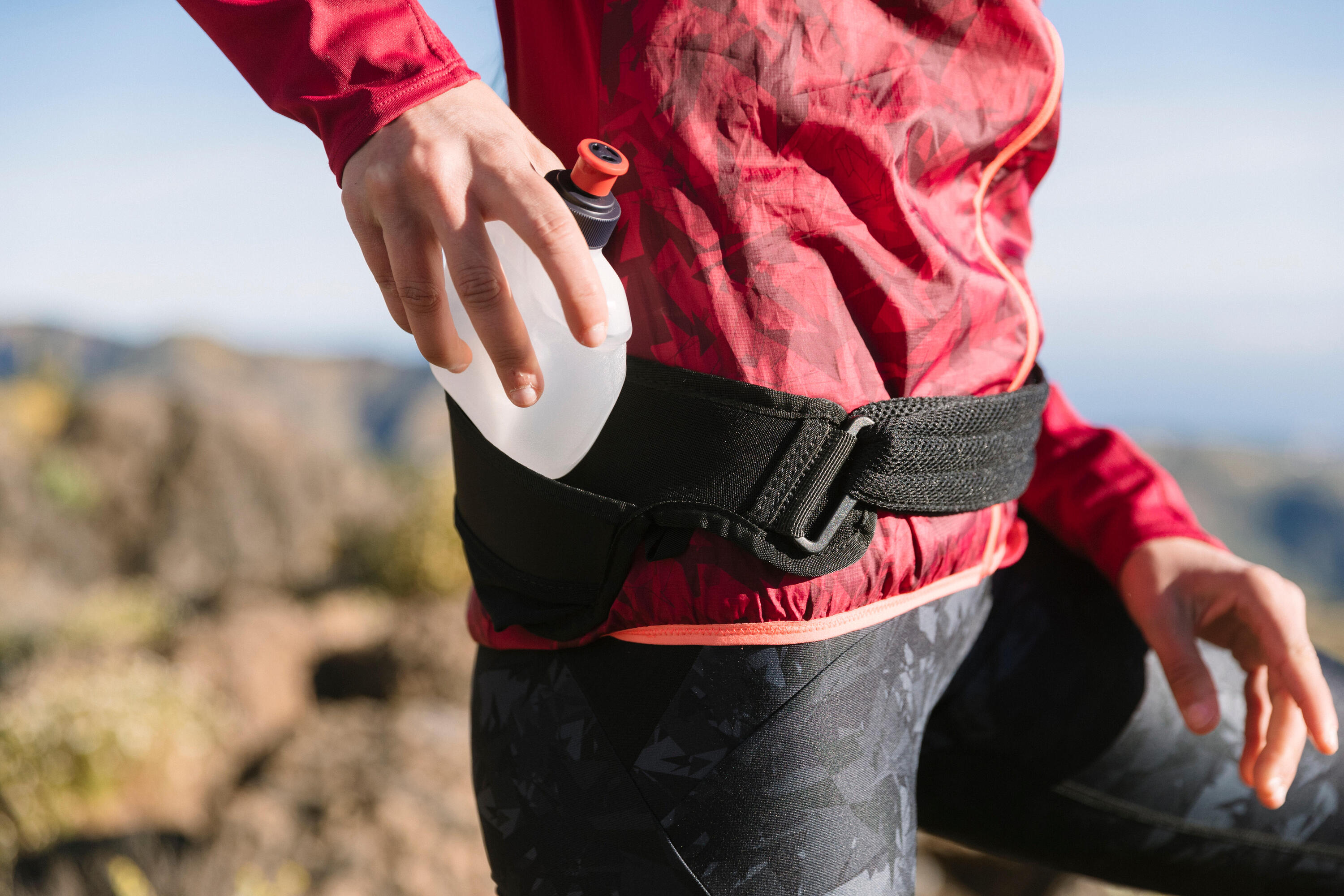 Close-up of a runner taking a soft water bottle from a black running belt, in a red jacket
