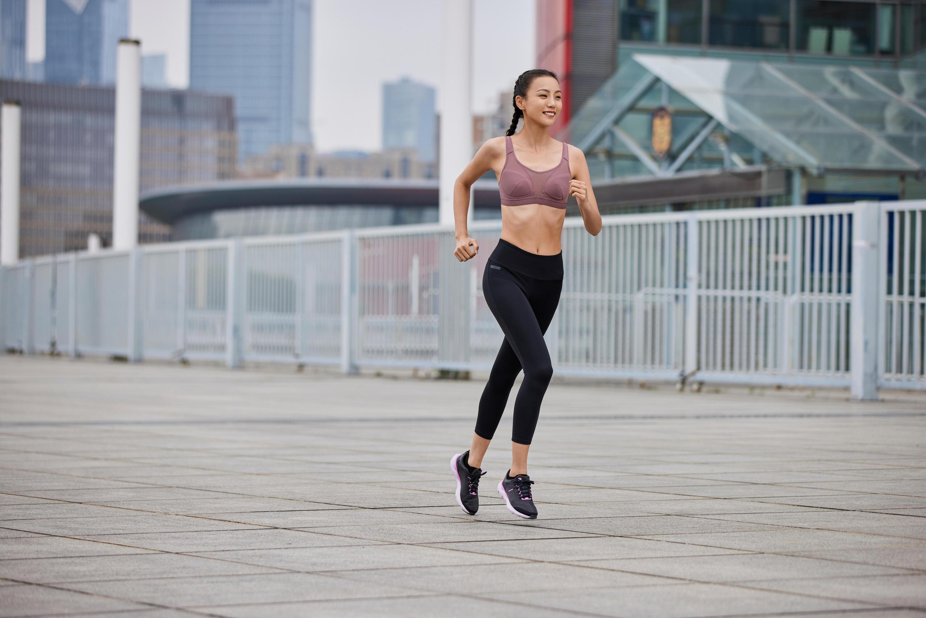 Woman running through a city plaza in a mauve sports bra and black leggings