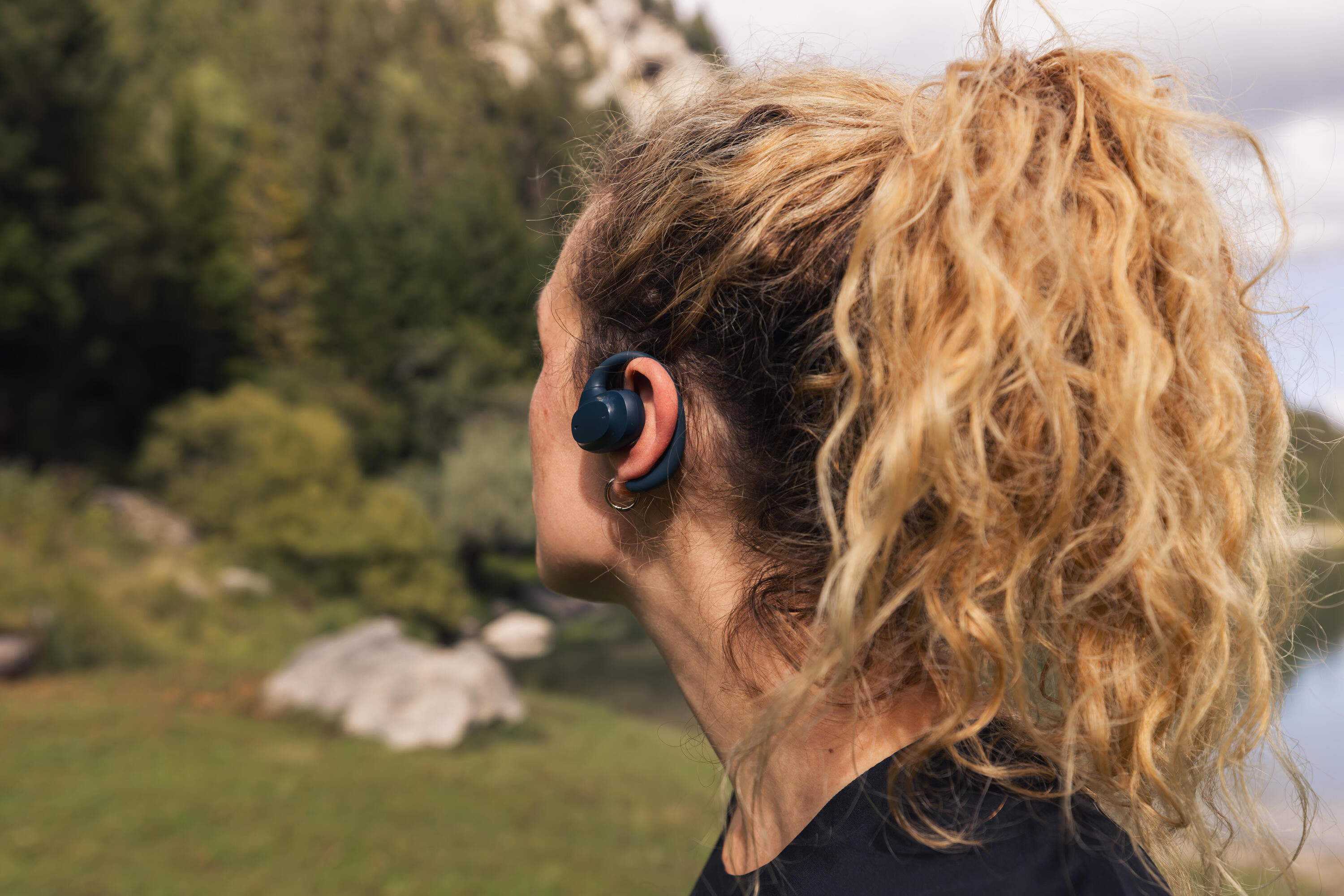 Close-up of a woman wearing a navy open-ear running earbud outdoors