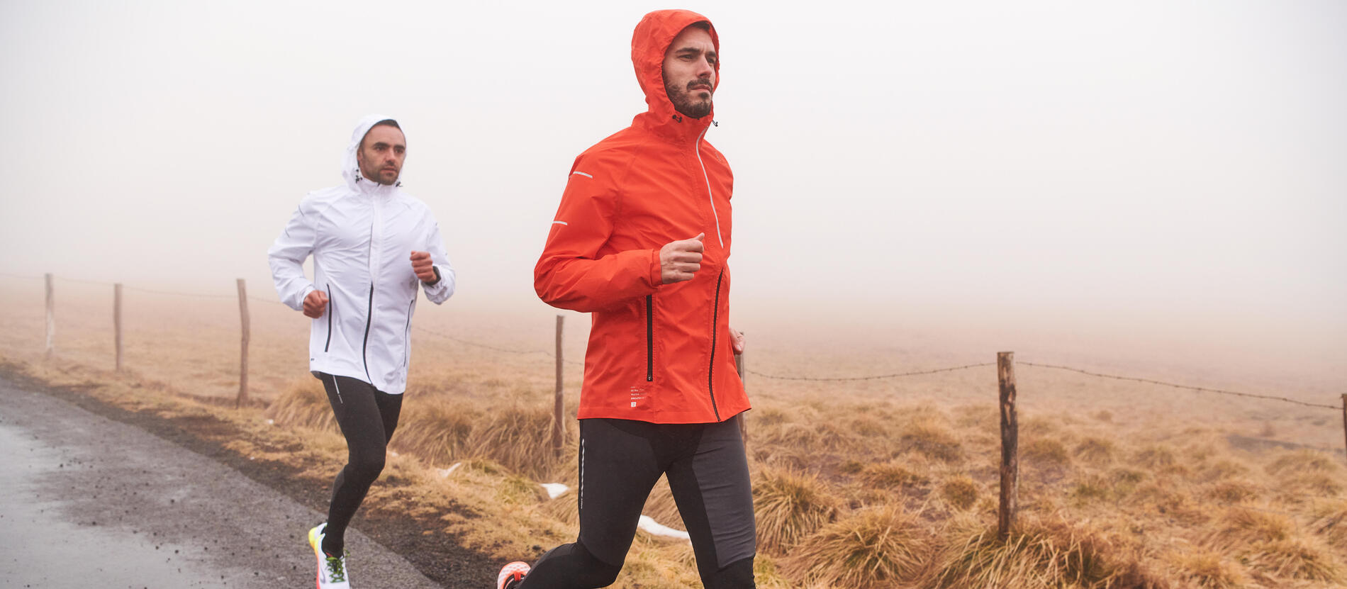 Two men running on a misty country road, one in an orange jacket and one in white