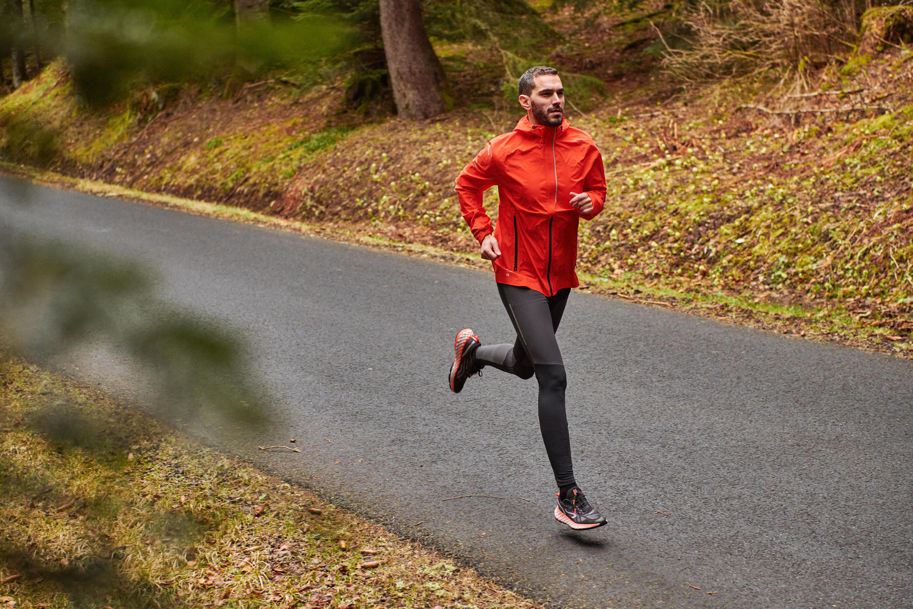 Man running on a forest road in the rain, in an orange waterproof jacket and black tights