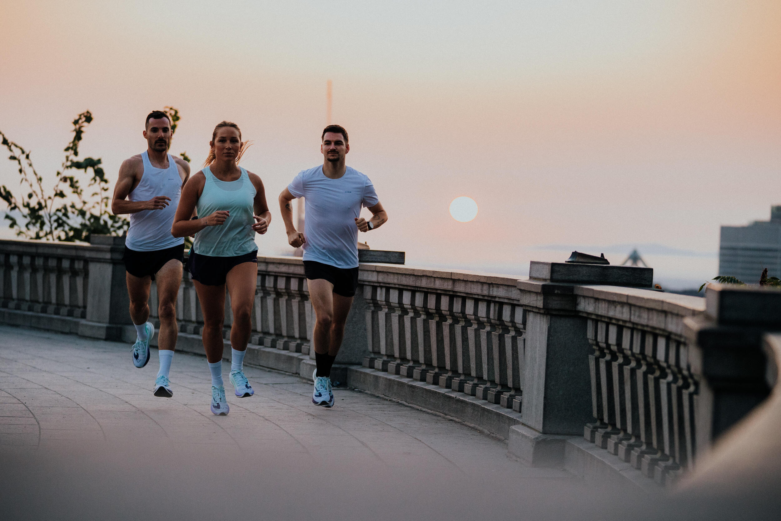 Three runners on a city bridge at sunset in vests and t-shirts