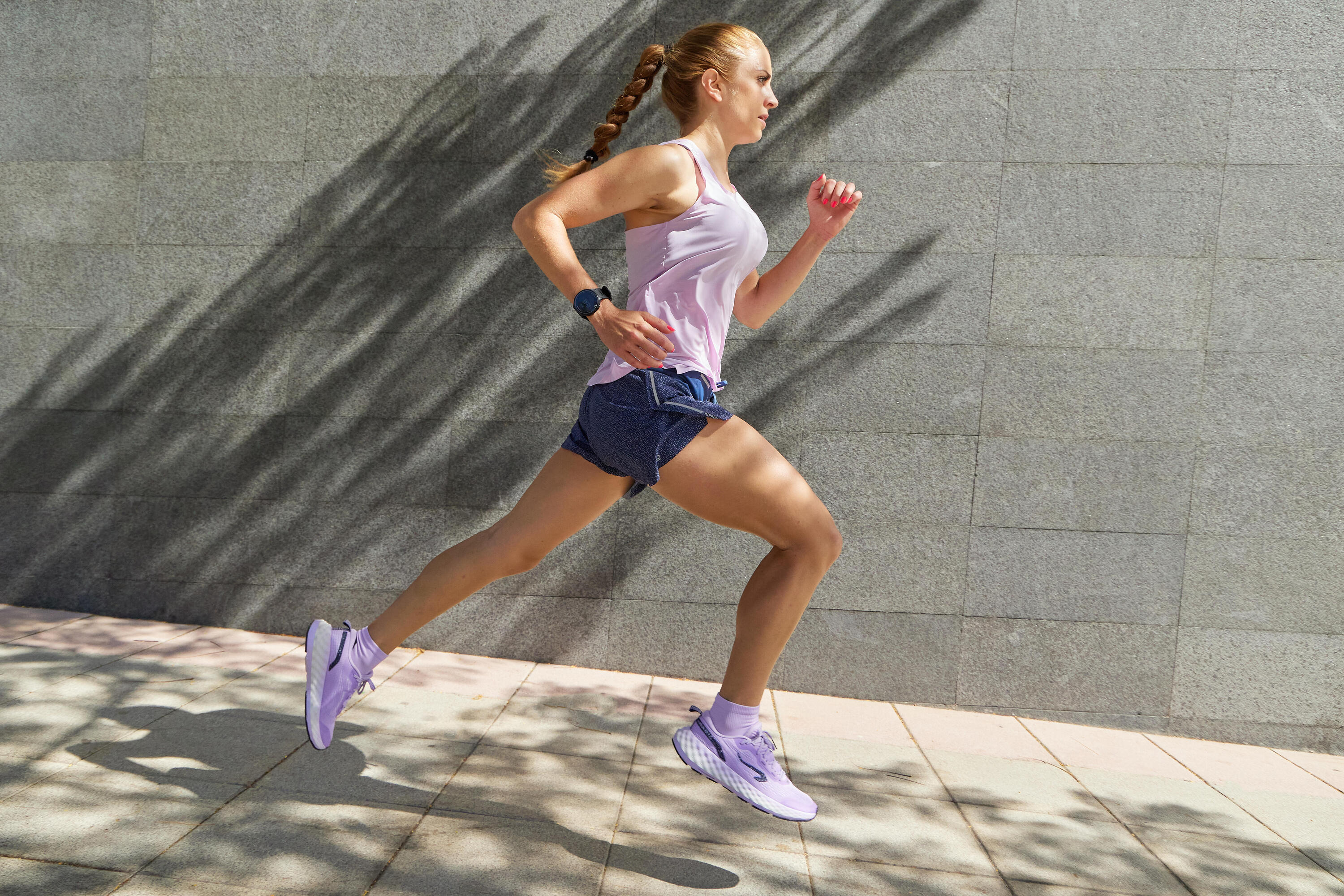 Woman running along a paved path in a lilac vest, navy shorts and lilac running shoes