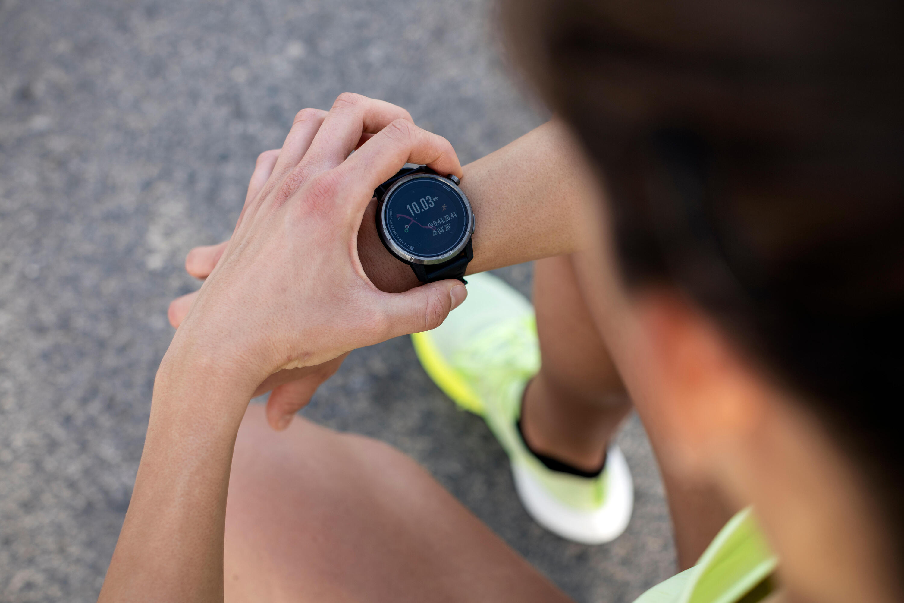 Close-up of a runner checking a GPS sports watch showing 10.03 km, with a green running shoe below