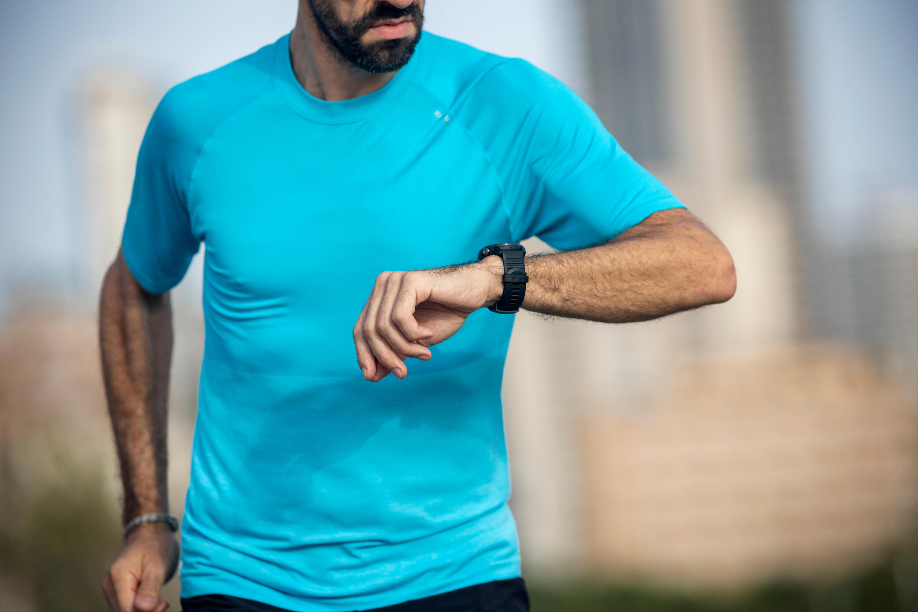Close-up of a man running outdoors in a blue t-shirt, checking his GPS watch