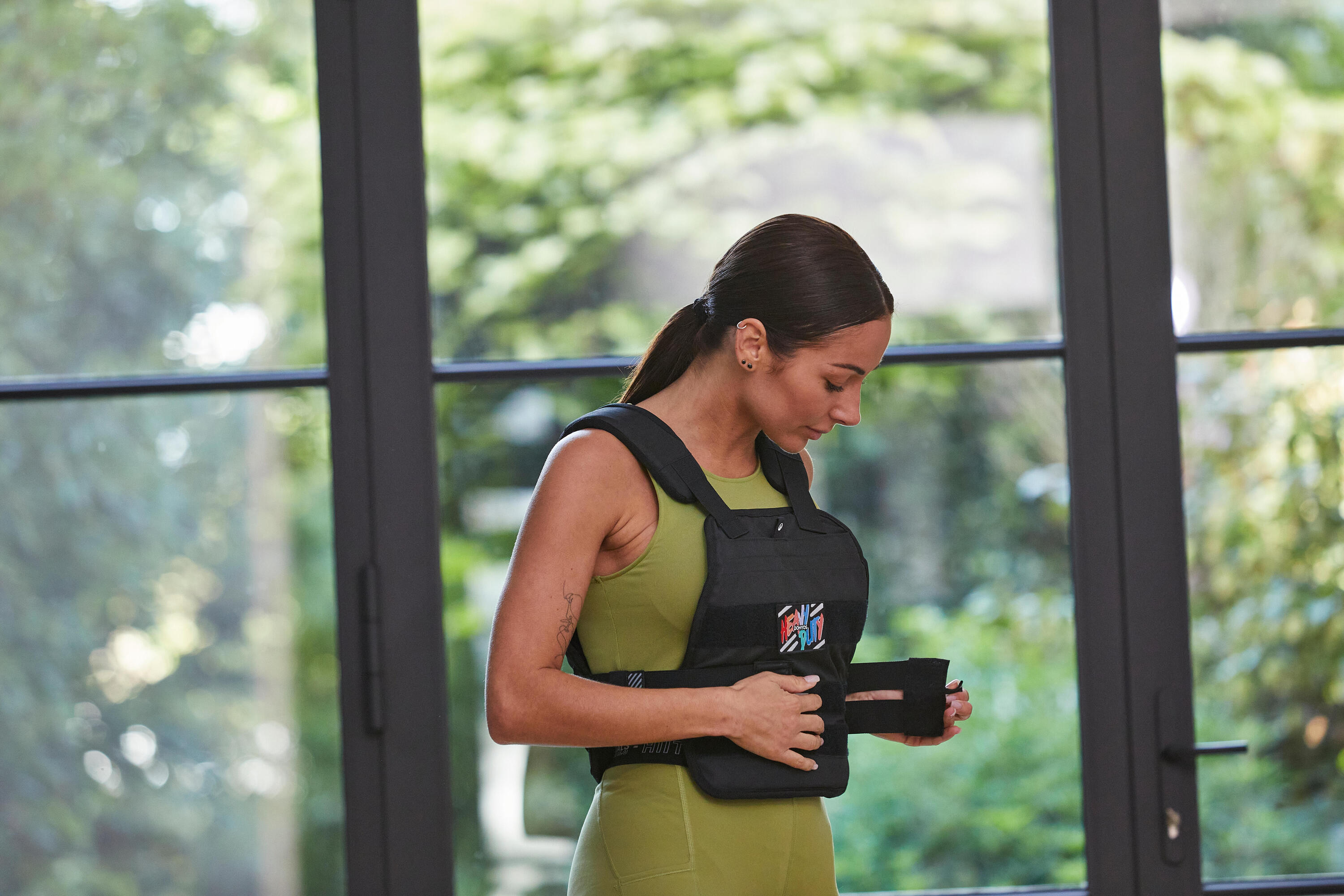 Woman fastening a black weighted training vest over a green workout outfit
